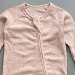 Close-up of the pink red spot print, the rib knit and the top of the zip
